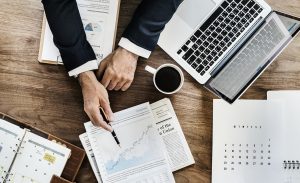 vue de dessus d'un bureau avec ordinateur portable tasse de café et homme qui montre des documents